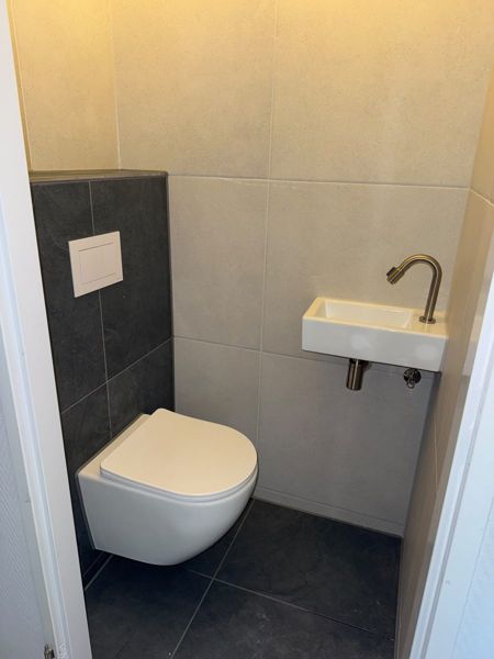 Toilet met antracieten wand, lichte tegels en messing kraan